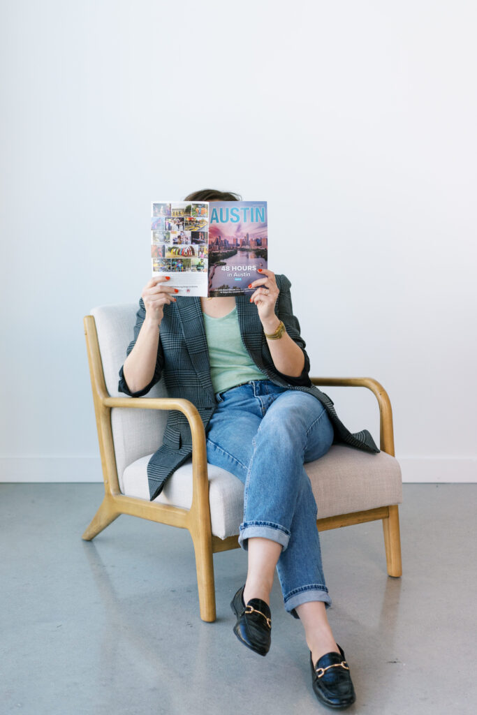 Kate sitting in a chair holding up a copy of the Austin Insider's Guide covering her face. 