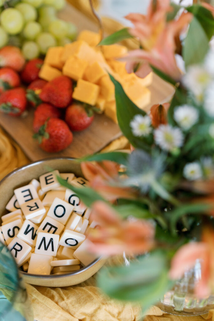 Fruit and flowers on a table with a bowl of scrabble tiles